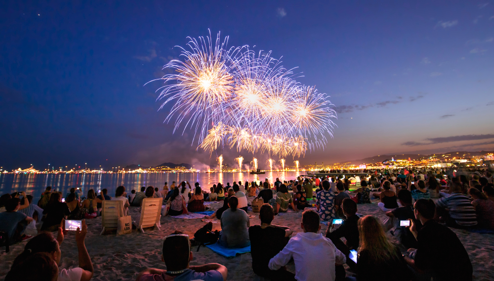 people on a beach watching fireworks over a lake